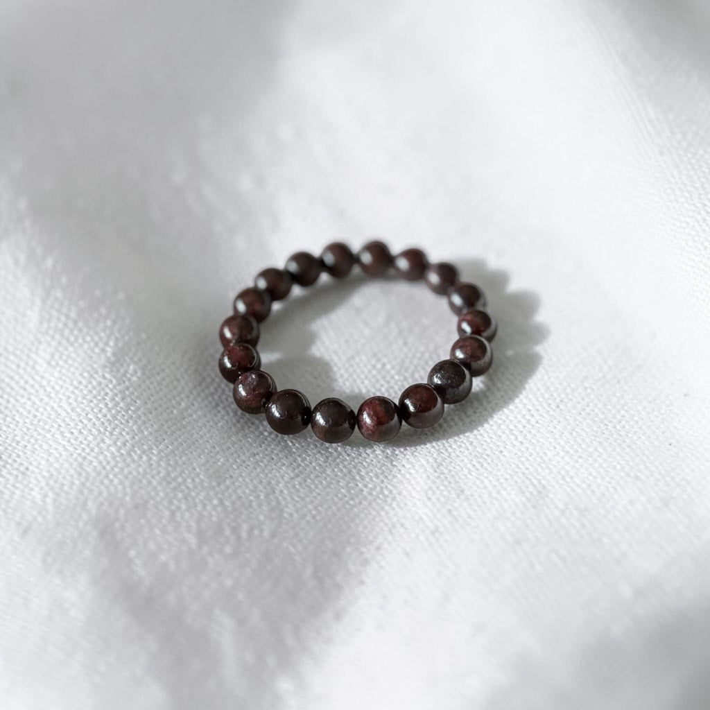 A beaded stretch bracelet made of small, polished dark brown wooden beads, resting on a textured white fabric background.
