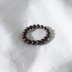 A beaded stretch bracelet made of small, polished dark brown wooden beads, resting on a textured white fabric background.