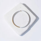 A delicate gold wire bracelet with a white beaded section, displayed on a textured white square tile against a clean white background.