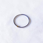 A thin purple blue wire seed bead bracelet with a small gold metal bead accent, displayed on a textured white fabric background.