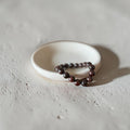 A beaded bracelet made of dark red  (brown feel) polished round beads, resting on a small white ceramic dish against a textured light gray concrete background.