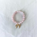 A pink beaded bracelet with a small gold bow charm, displayed on a textured white fabric background.