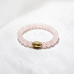 A beaded stretch bracelet made of light pink rose quartz beads with a central gold-colored metallic bead, resting on a white textured fabric background.