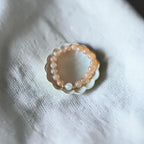 A beaded stretch bracelet with peach-orange translucent beads and a white pearl accent, displayed on a small white scalloped dish over a textured white fabric background.