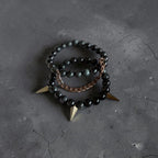 Two beaded bracelets with black beads and gold-toned spikes, one with a rose gold chain link, displayed on a dark textured surface.