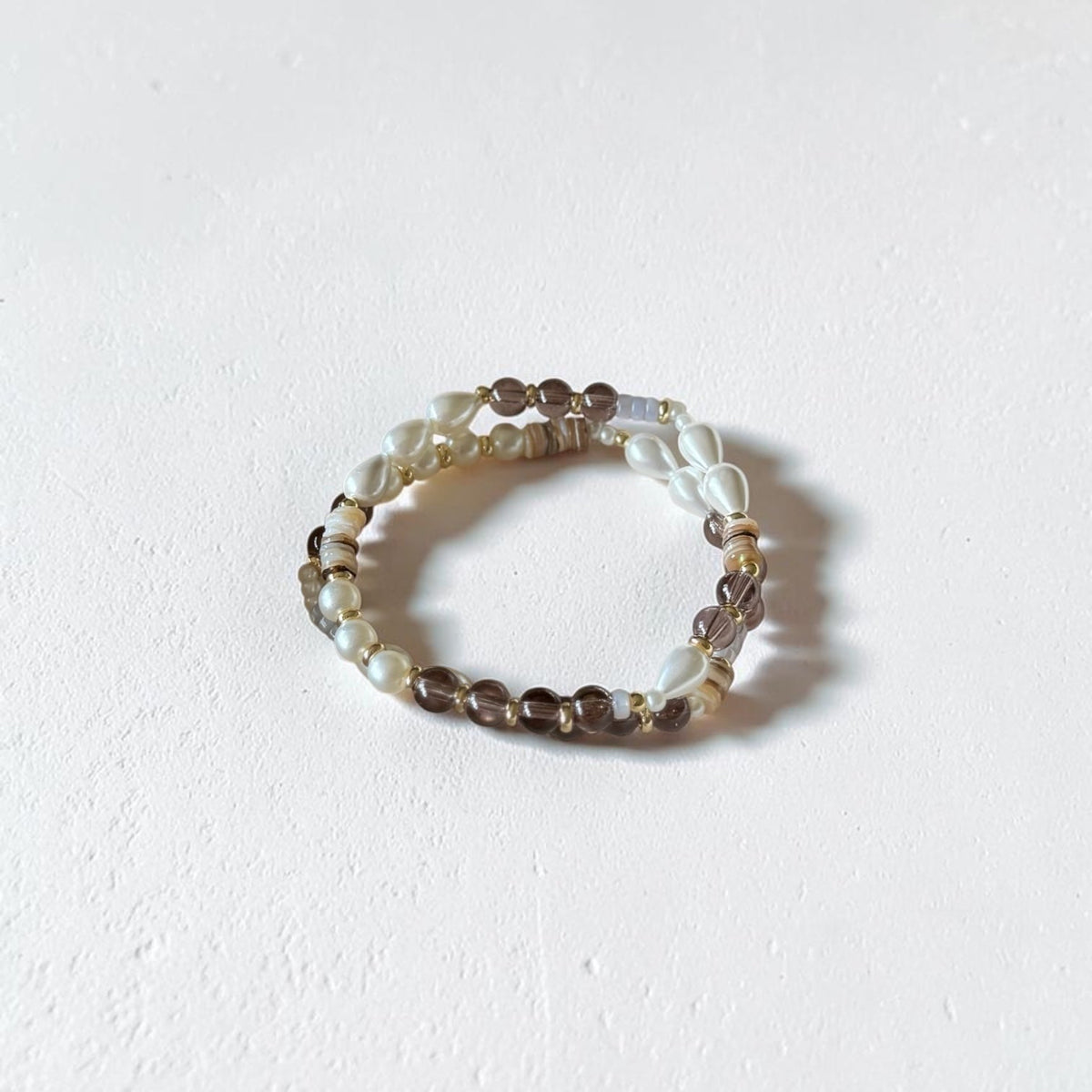 A beaded stretch bracelet featuring white, translucent, and brown beads, photographed on a textured off-white surface.