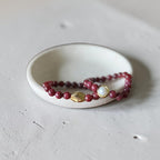 2 8mm Red Garnet Jade Bead Bracelet with a Gold And Pearl Accent and one wiht gold accent. Accent has a round pearl with gold surrounding the pearl itself. This bracelet is sitting in a dish.
