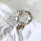A beaded ring featuring clear, round glass beads and a small gold bow charm, resting on a textured white fabric background.