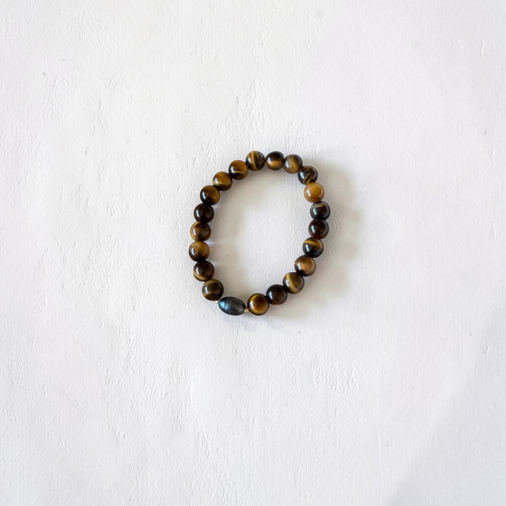 A beaded stretch bracelet made of polished tiger's eye and obsidian beads, arranged in a circle on a textured white background.