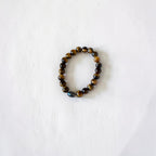 A beaded stretch bracelet made of polished tiger's eye and obsidian beads, arranged in a circle on a textured white background.