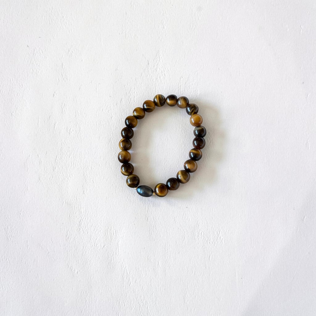 A beaded stretch bracelet made of polished tiger's eye and obsidian beads, arranged in a circle on a textured white background.