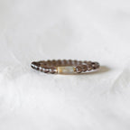 A beaded bracelet with dark brown textured beads and a central rectangular cream-colored stone, resting on a soft white fabric background.