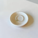 A small handmade ceramic dish with a speckled off-white glaze, featuring a textured circular pattern in the center, set on a plain white surface.