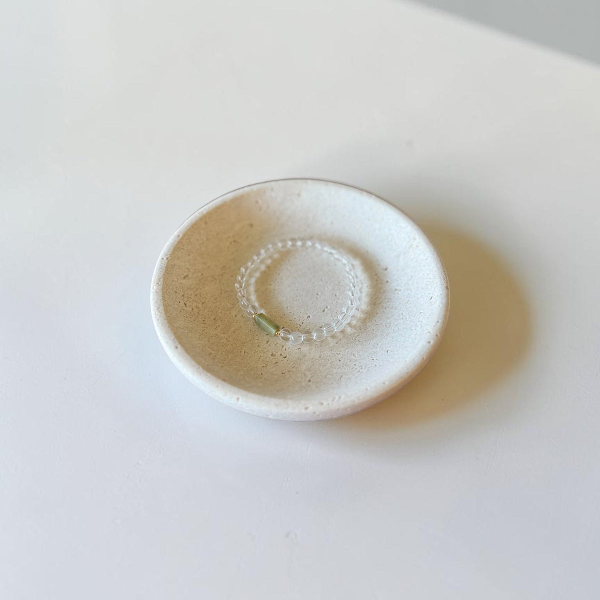 A small handmade ceramic dish with a speckled off-white glaze, featuring a textured circular pattern in the center, set on a plain white surface.