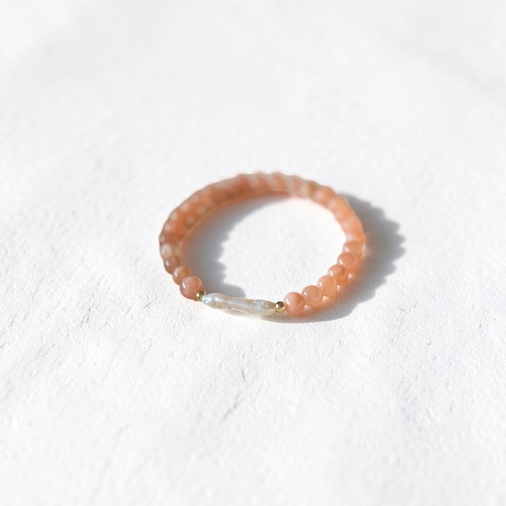 A peach-orange beaded bracelet with a small white stone accent, photographed on a textured white surface with a soft shadow.