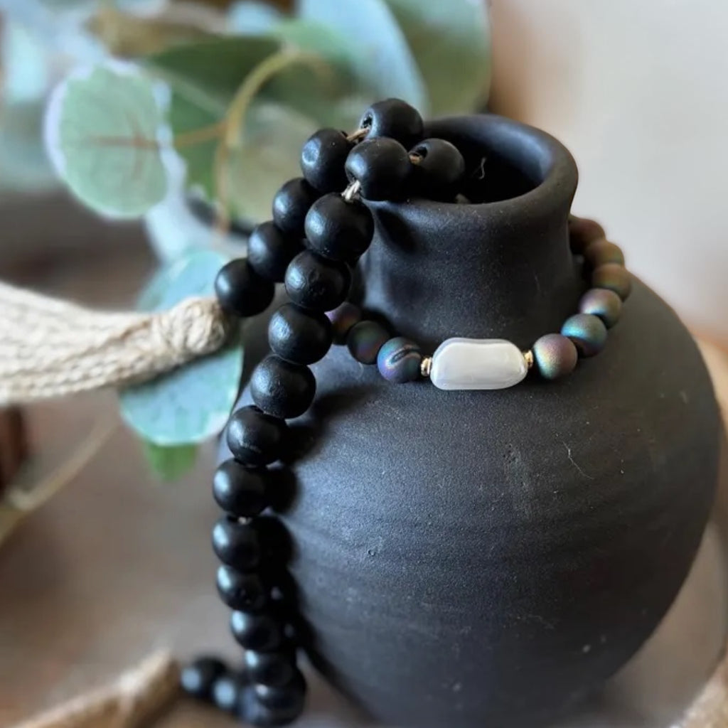 A beaded bracelet draped over a matte black ceramic vase.