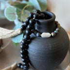 A beaded bracelet draped over a matte black ceramic vase.