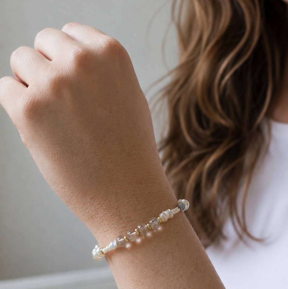 A delicate beaded bracelet with white pearls and clear beads worn on a woman's wrist, shown in a close-up lifestyle shot.