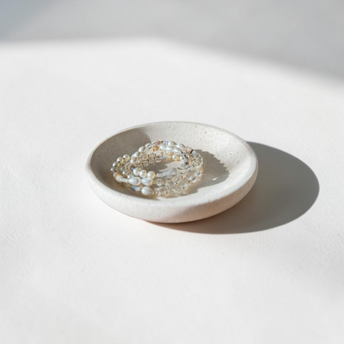 A mixture of clear quartz, pearl stones 6mm bracelets. Bracelets are stacked sitting in a dish. 