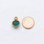 The bracelet charm with jump hoop. Outlined in gold and a stone inside. Sitting next to a penny on white texture background. Showing the comparison of the size. 
