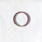 A thin red leather bangle bracelet with a small gold bead accent on one side, displayed on a white marble surface.