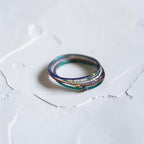 A delicate multi-layered ring with colorful glass strands, tiny white pearls, and small gold beads, resting on a textured white surface.