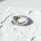 Two bracelets stacked on a white texture background. Blue Fire Agate Beads with a mixture of other accents. Pearls, Gold Plated Spacers.
