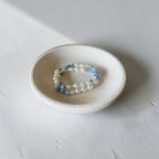 The Jodi Bracelet — Blue Fire Agate, Moonstone, and pearl stretch bracelet by Poppies & Jules. These bracelets are sitting in a dish with lighting shining on it.