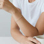 A delicate wire bracelet worn on a woman's wrist, shown in a lifestyle setting with her hands resting on a white table next to a mug.