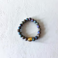 A beaded stretch bracelet made of iridescent dark beads with a central gold-toned spacer bead, displayed on a textured off-white surface.