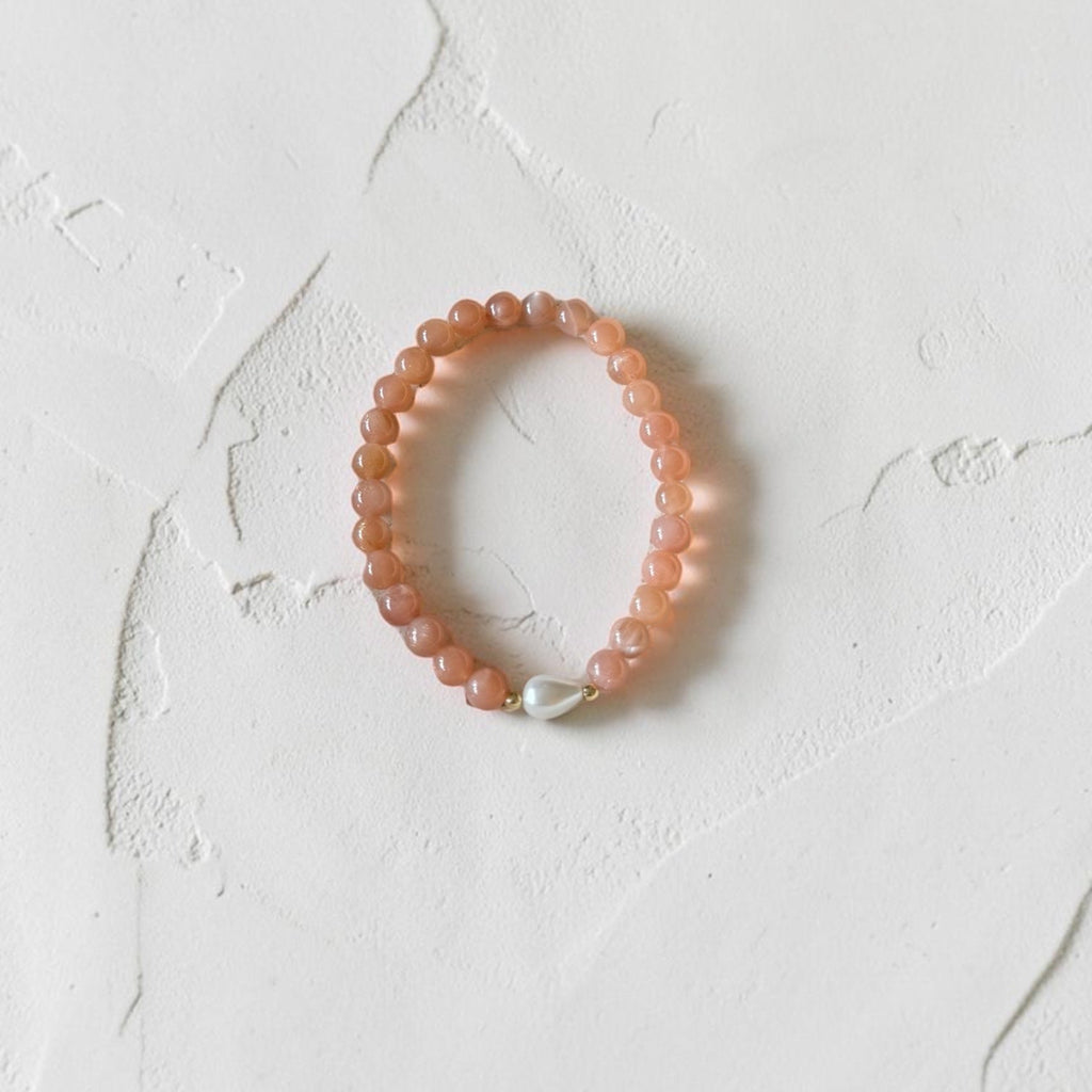 A peach-colored beaded bracelet with a small white pearl accent, displayed on a textured off-white surface.