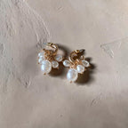 A pair of gold hoop earrings with dangling clusters of white freshwater pearls, displayed on a textured beige surface.