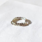 A beaded stretch bracelet featuring small white pearls and brown smoky crystal beads, resting on a textured white surface with a soft shadow.