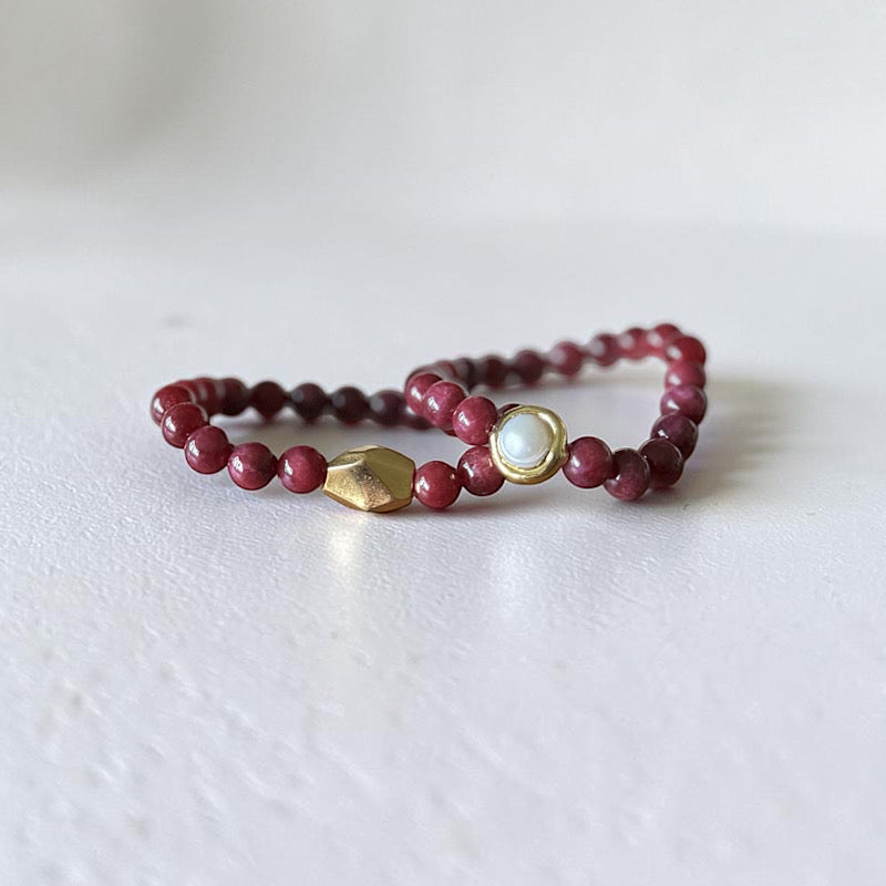 2 8mm Red Garnet Jade Bead Bracelet with a Gold And Pearl Accent and gold accent. Accent has a round pearl with gold surrounding the pearl itself. This bracelet is sitting in a dish.