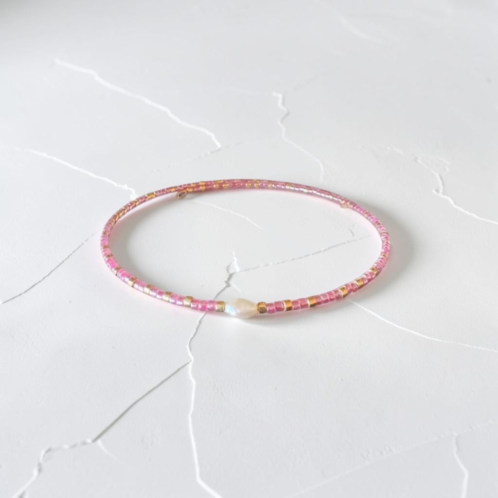 A delicate pink beaded bracelet with small gold and white accents, resting on a white textured surface.
