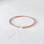 A delicate pink beaded bracelet with small gold and white accents, resting on a white textured surface.
