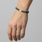 A beaded bracelet with dark teal-blue beads and a central white pearl, shown worn on a person's wrist against a plain light gray background.