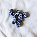 A cluster of small, irregularly shaped beads with a blue and white leaf-like pattern, resting on a textured white fabric background.