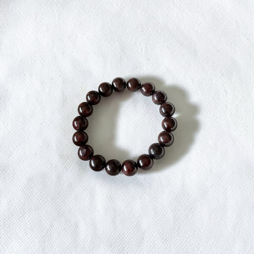 A dark brown beaded bracelet made of polished round beads, arranged in a circle on a textured white fabric background.