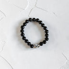 A beaded stretch bracelet made of glossy black round beads with a small white and black spotted accent bead, displayed on a textured white surface.