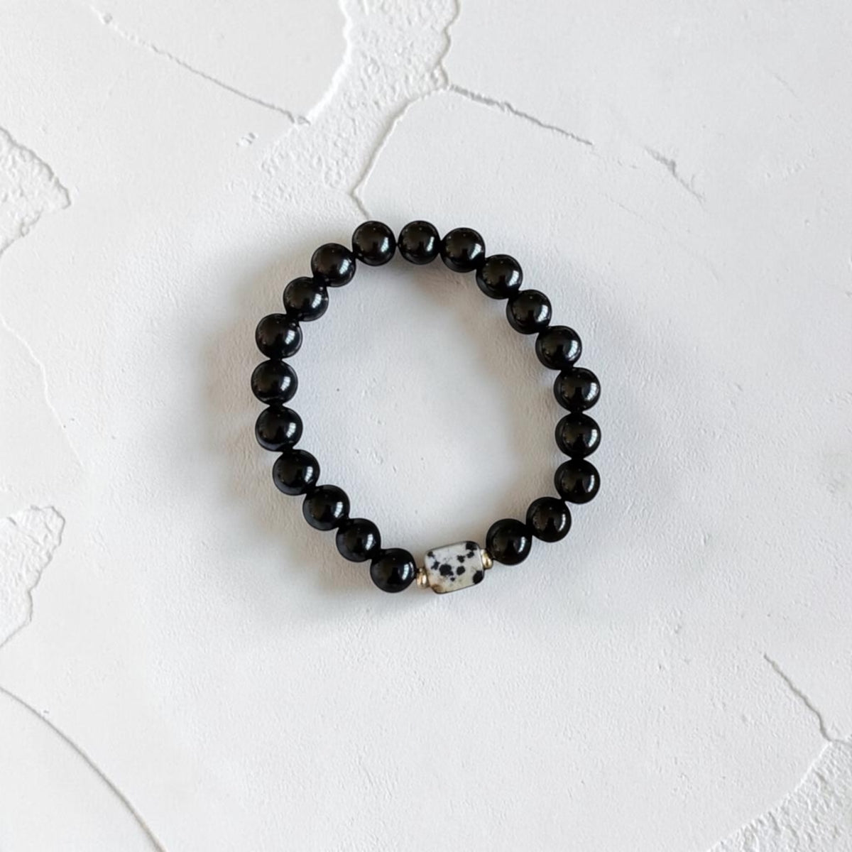 A beaded stretch bracelet made of glossy black round beads with a small white and black spotted accent bead, displayed on a textured white surface.