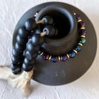 A bbeaded bracelet featuring iridescent purple, blue, and green beads with gold spacer rings, set against a textured off-white background.