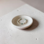 A delicate beaded stretch bracelet with white pearls and light blue beads, displayed on a small white ceramic dish.