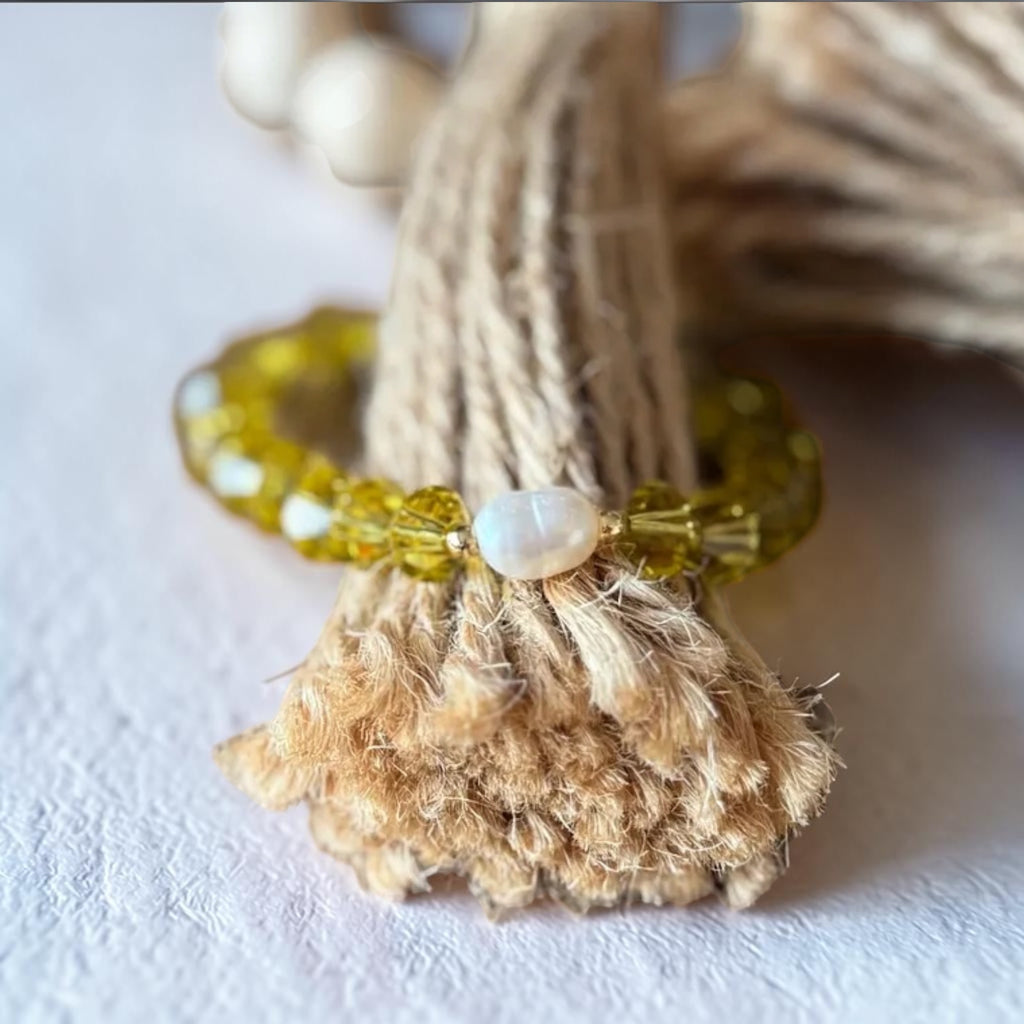 A beaded bracelet with translucent yellow-green beads and a central white pearl, displayed wrapped around a textured beige jute bundle on a light surface.