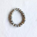 A beaded stretch bracelet made of round white beads with black speckles, accented by a few metallic gold spacer beads, displayed on a textured white surface.