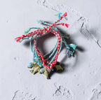 A set of handmade multicolor braided string bracelets with small gold-toned charms, displayed on a textured light gray surface.