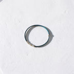 A thin beaded bracelet with dark teal-blue beads and small white pearl-like accents, photographed on a textured white surface with a soft shadow.