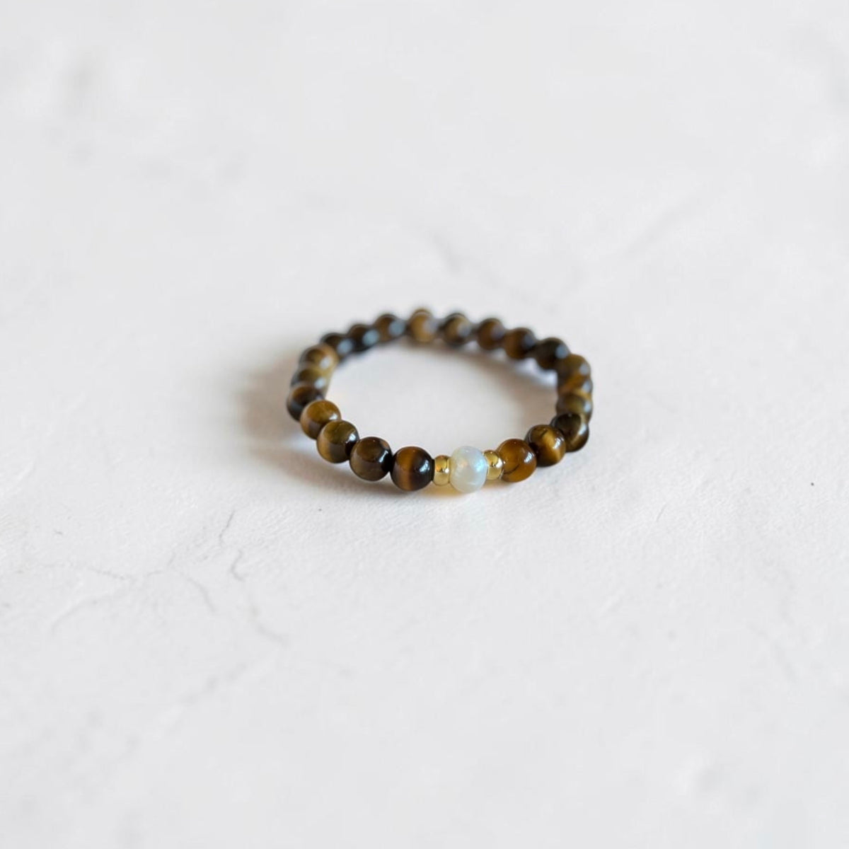 A beaded stretch bracelet featuring brown and black tiger's eye beads with a small light blue stone accent, resting on a textured white surface.