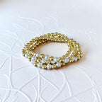 A stack of three beaded stretch bracelets, featuring alternating sections of shiny gold metallic beads and textured silver glitter beads, displayed on a white embossed background.