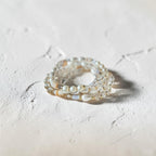A stack of three beaded rings featuring white pearls, clear faceted beads, and small iridescent shell accents, displayed on a textured light beige surface.